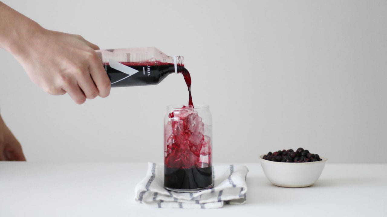 Arepa drink being poured from a bottle to glass. A bowl of blackcurrants stand alongside
