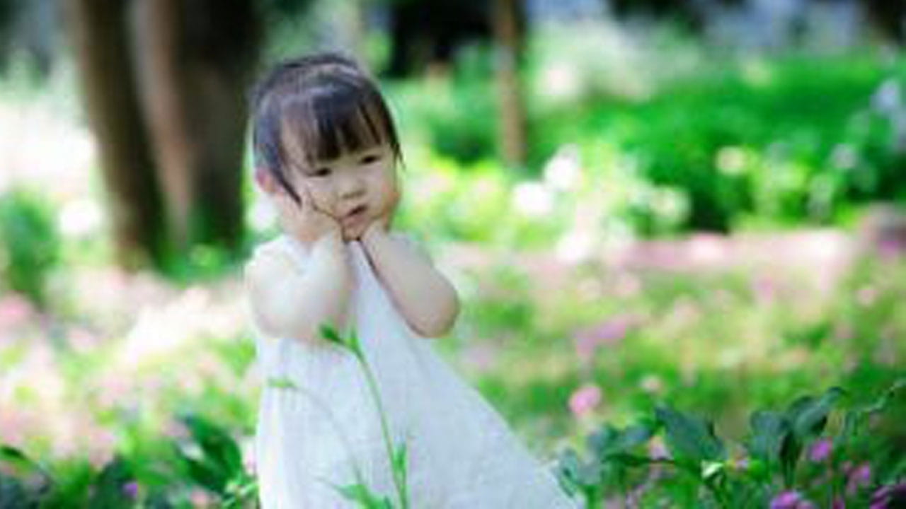 Female preschool aged girl in a white dress standing in a meadow