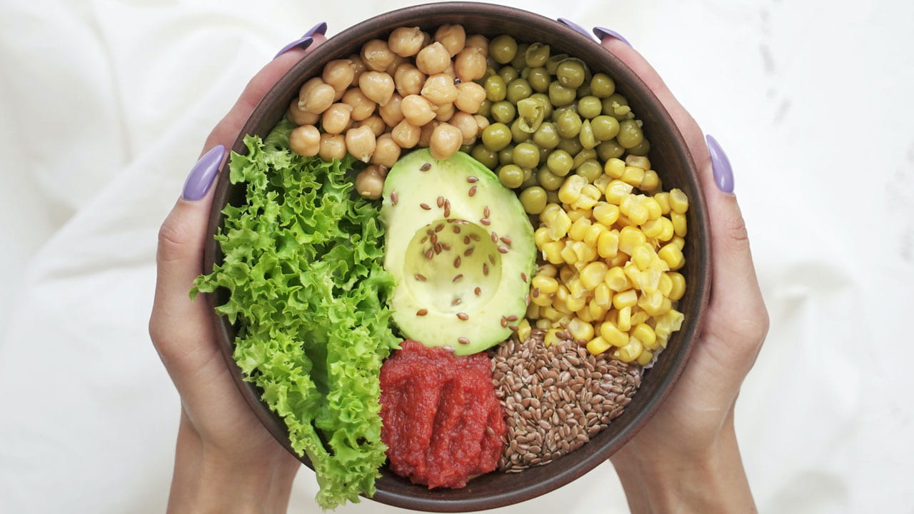 woman's manicured hands holding brown bowl containing salad, legumes and seeds
