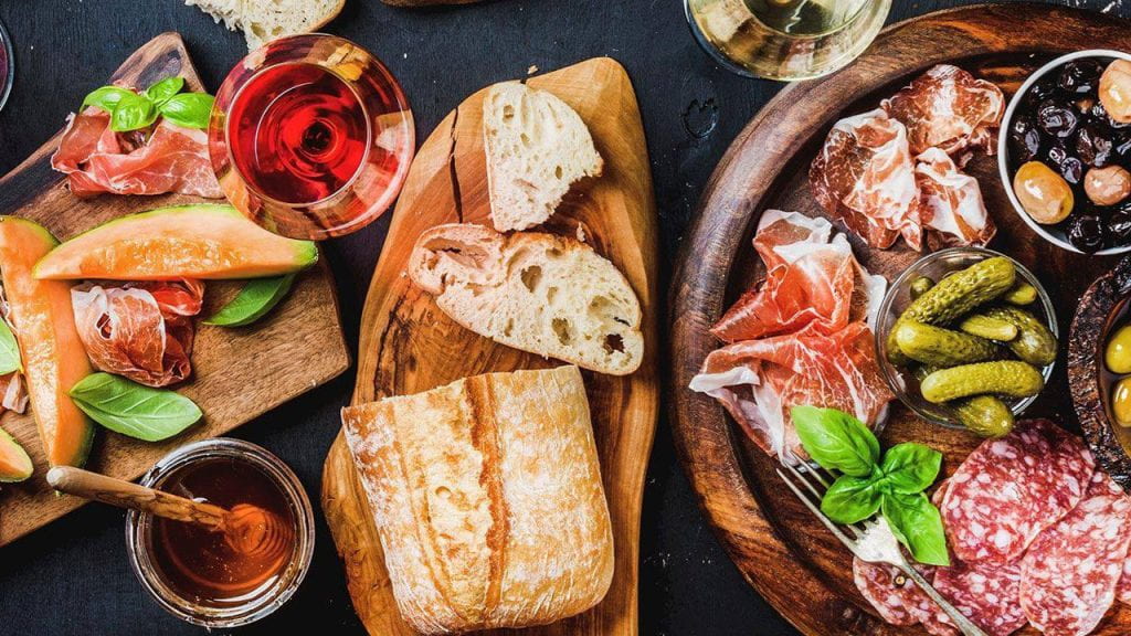 Antipasto, fruit, bread, honey and wine on wooden serving boards