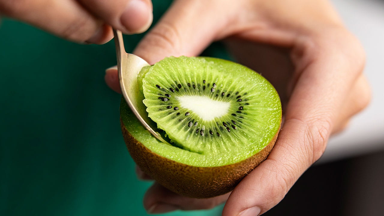 Half a green kiwifruit and a spoon being held in a hand